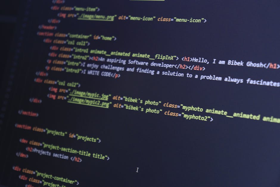 Photograph showing a close-up of a computer screen displaying lines of HTML and CSS code in various colors, including blue, yellow, red, and green. The code contains tags, attributes, and comments rel
